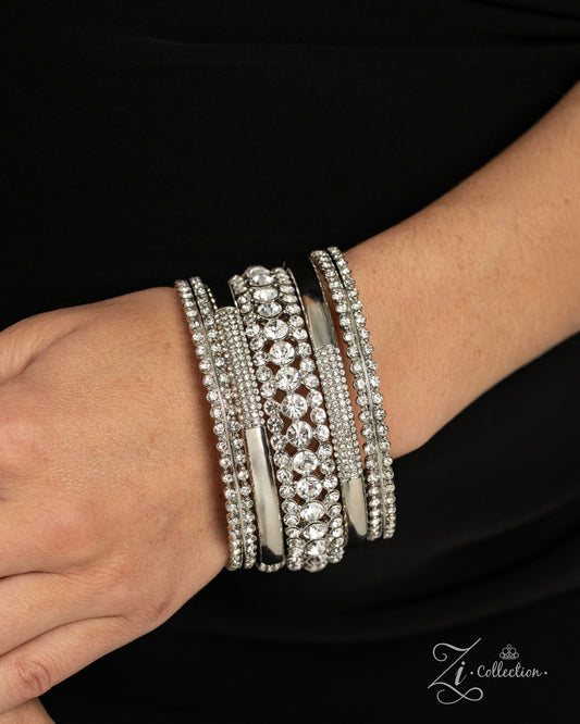 A close-up of a person's wrist wearing a stack of wide silver bangles adorned with clear rhinestones and crystal-like stones, set against a black top background. A 'Zi Collection' logo watermark is visible in the bottom right corner.
