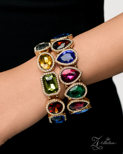 A close-up of a person's wrist wearing a stack of three gold-toned bangle bracelets, each adorned with large, colorful gemstone clusters in shades of blue, green, yellow, red, and purple. The background is a solid black fabric.