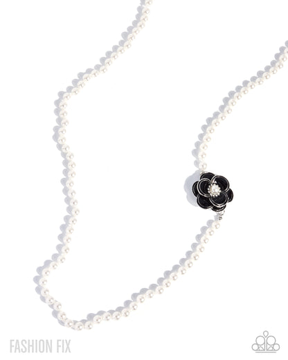 A white pearl necklace with a black flower-shaped charm featuring a clear crystal center, displayed on a clean white background with soft shadows.