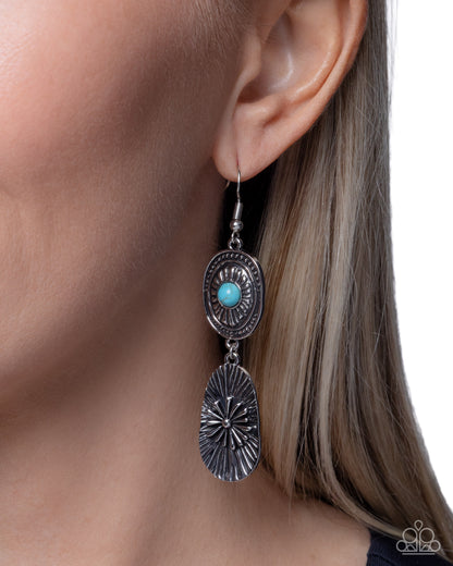 Silver earring with turquoise stone worn by a person on a neutral background