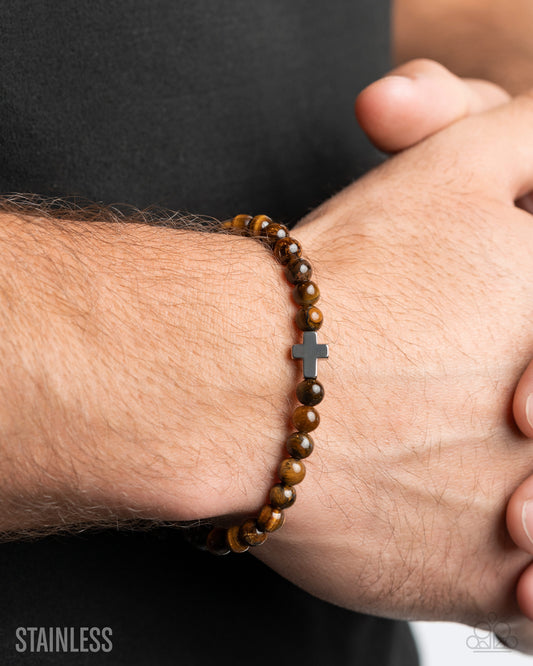 Brown beaded bracelet with a silver cross on a wrist against a dark background
