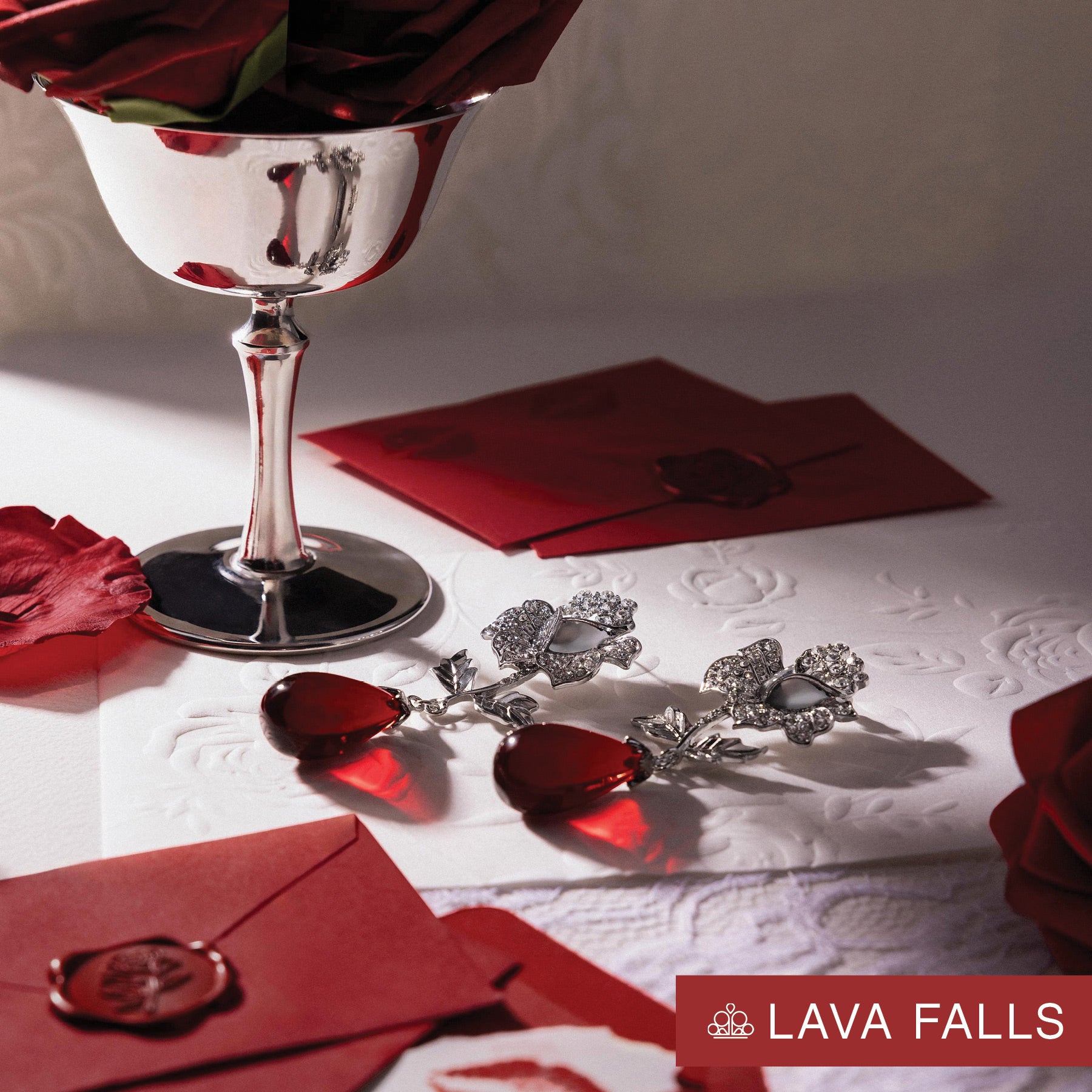 Silver earrings with red stones on a white surface with red roses and envelopes, LAVA FALLS brand visible.