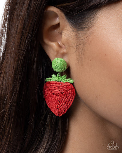 Red strawberry-shaped earring with green leaves worn by a person