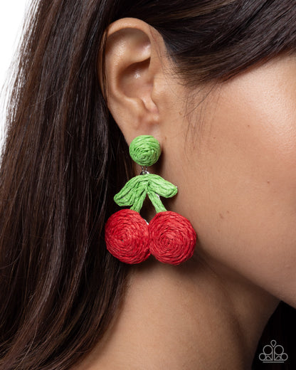 Close-up of a person wearing red and green cherry-shaped earrings.