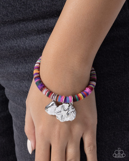 Multicolored striped bracelet with silver charms on a wrist against a black background