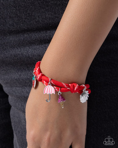 Red braided bracelet with charms on a wrist against a dark background