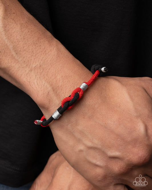 Bracelet with red and black cord on a wrist against a dark background