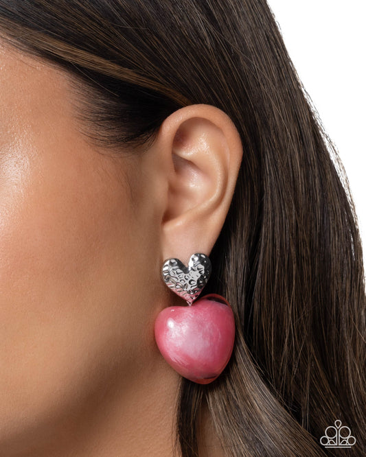 Pink heart-shaped earring worn by a model on a white background