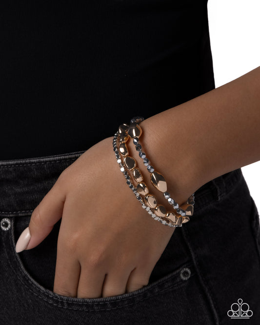 Hand wearing a stack of gold and silver bracelets on a black background