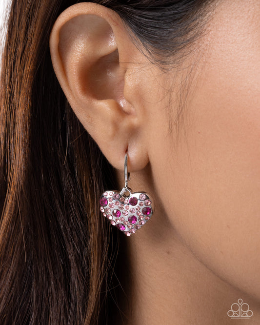 Heart-shaped earring with pink and purple stones worn by a person
