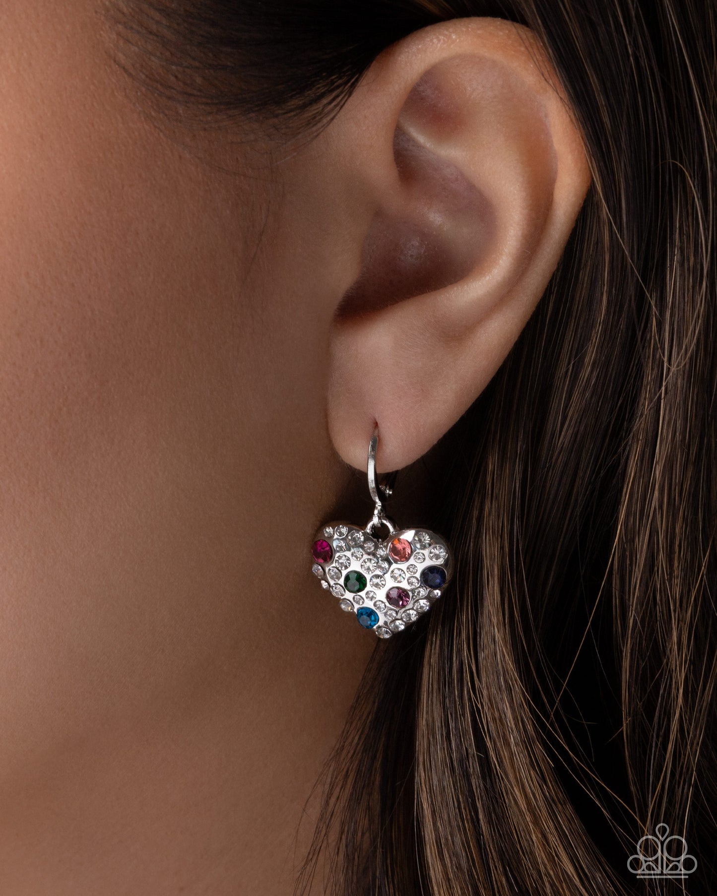 Heart-shaped earring with colorful gemstones worn by a person
