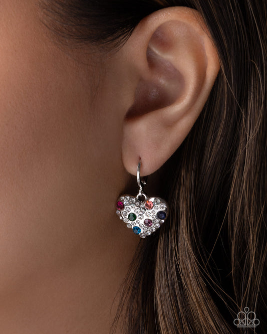 Heart-shaped earring with colorful gemstones worn by a person