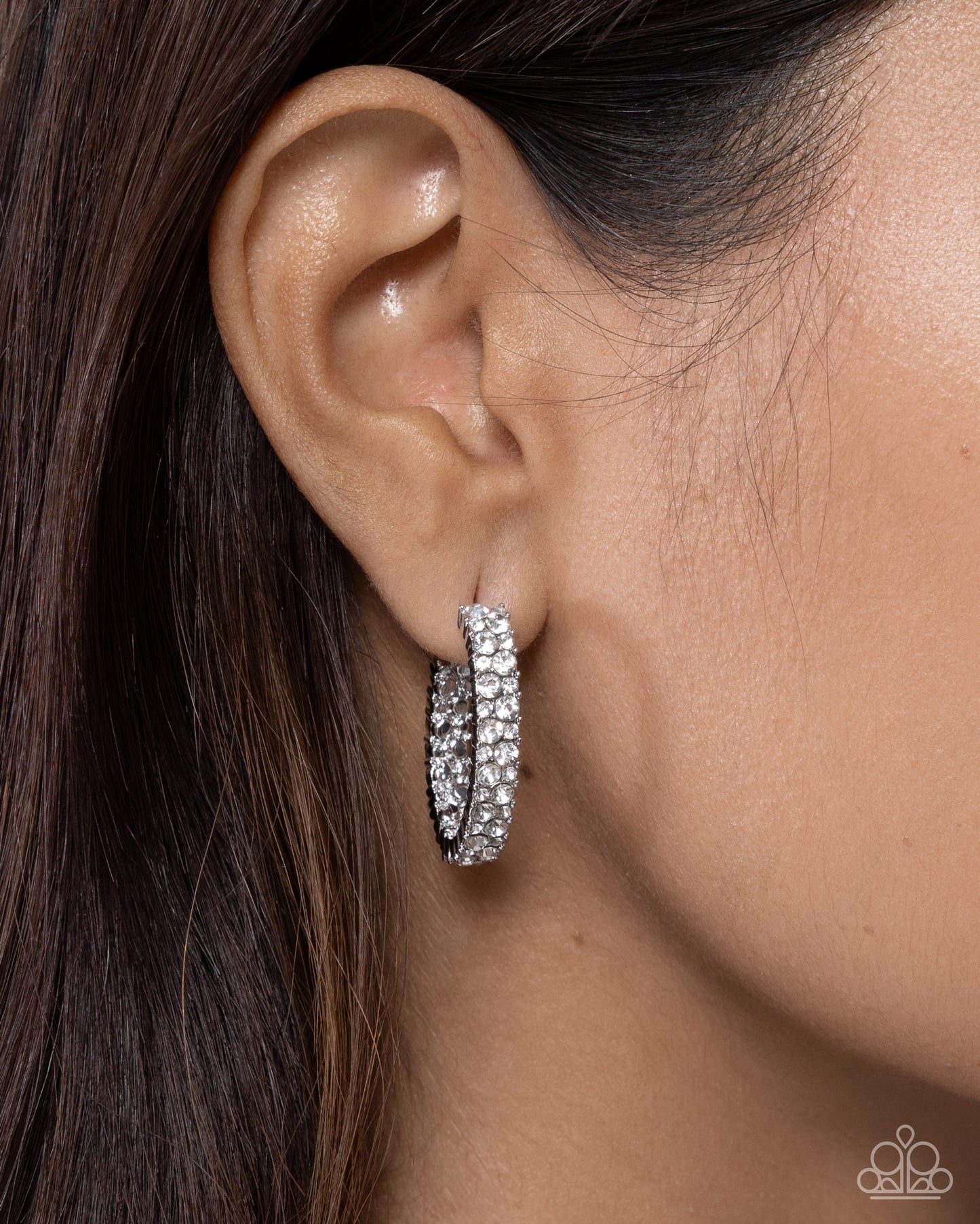 Close-up of an ear wearing a silver hoop earring with a blurred background