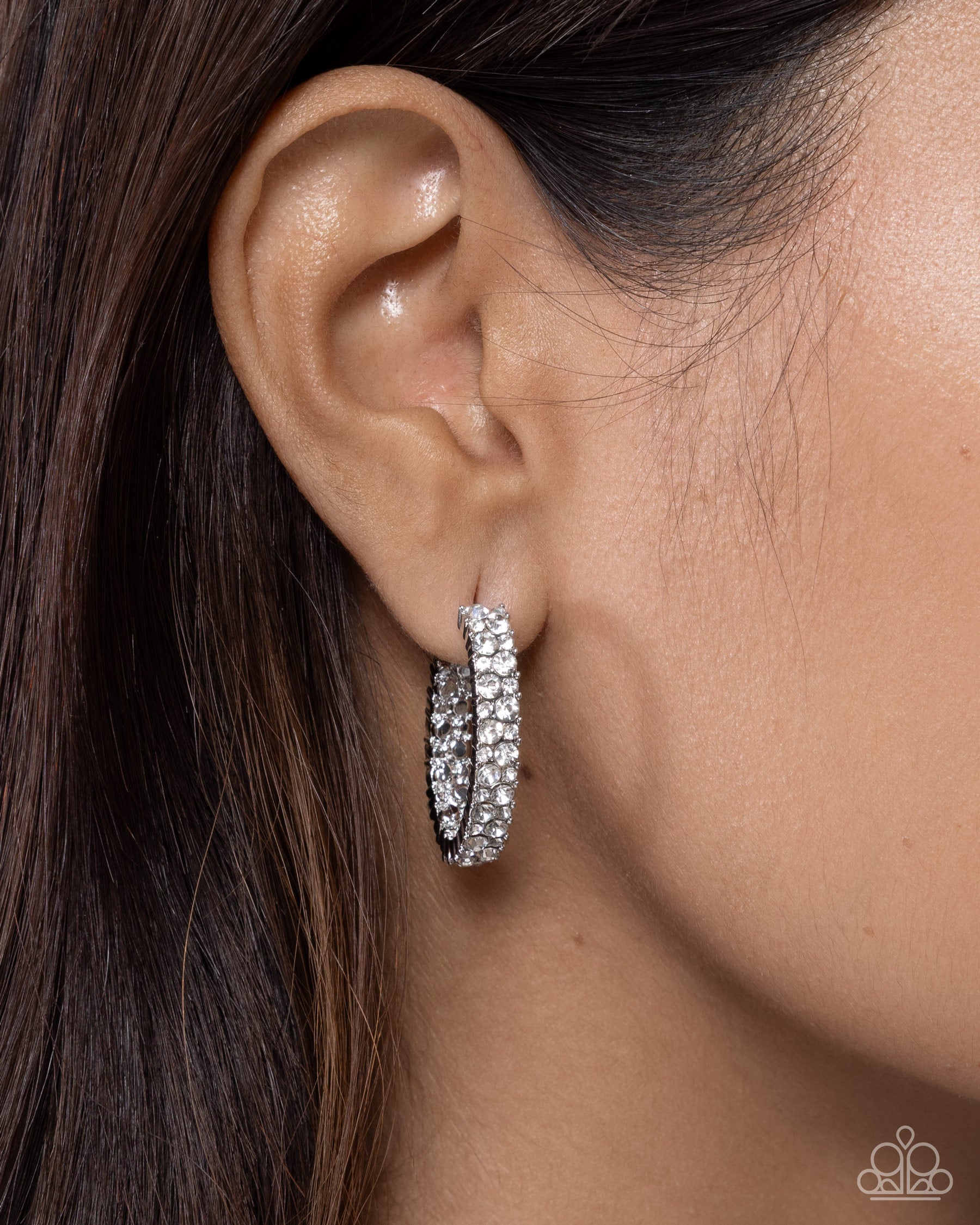 Close-up of an ear wearing a silver hoop earring with a blurred background