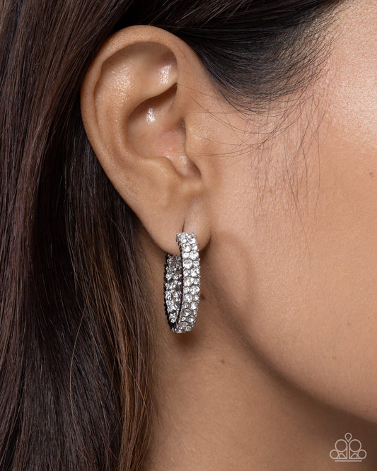 Close-up of an ear wearing a silver hoop earring with a blurred background