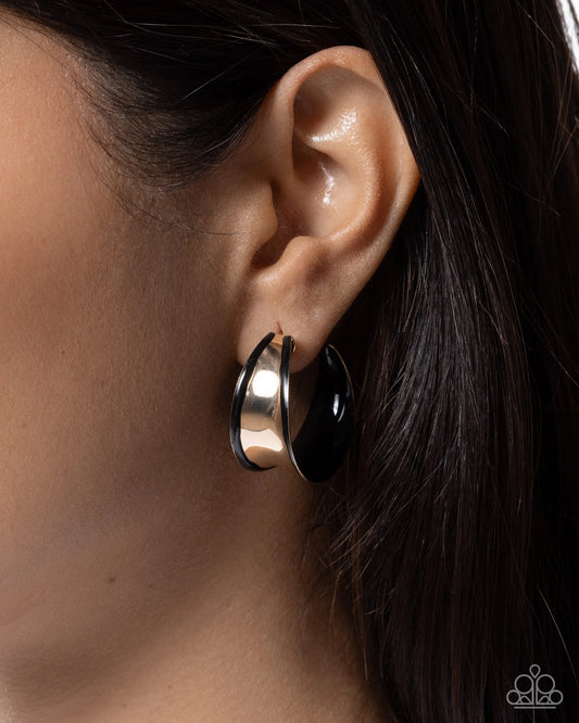 Close-up of an ear wearing a gold hoop earring with a black center.