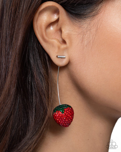 Close-up of an ear wearing a red strawberry-shaped earring with a green leaf on a neutral background