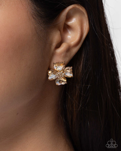 Gold and crystal flower earring worn by a person with dark hair.
