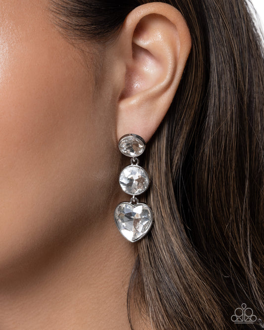 Close-up of an ear wearing a silver earring with heart-shaped gemstones.