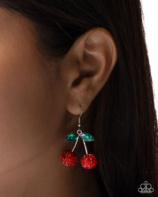 Close-up of an ear wearing a red and green cherry earring with dark hair in the background.