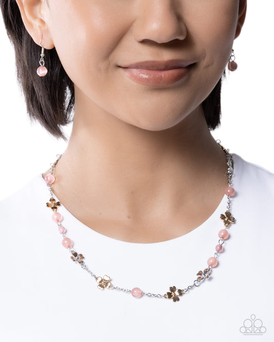 Necklace with pink beads and floral elements worn by a model on a white background