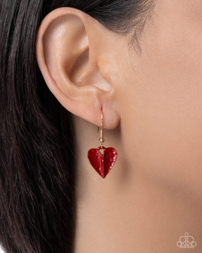 Red heart-shaped earring worn by a model with dark hair.