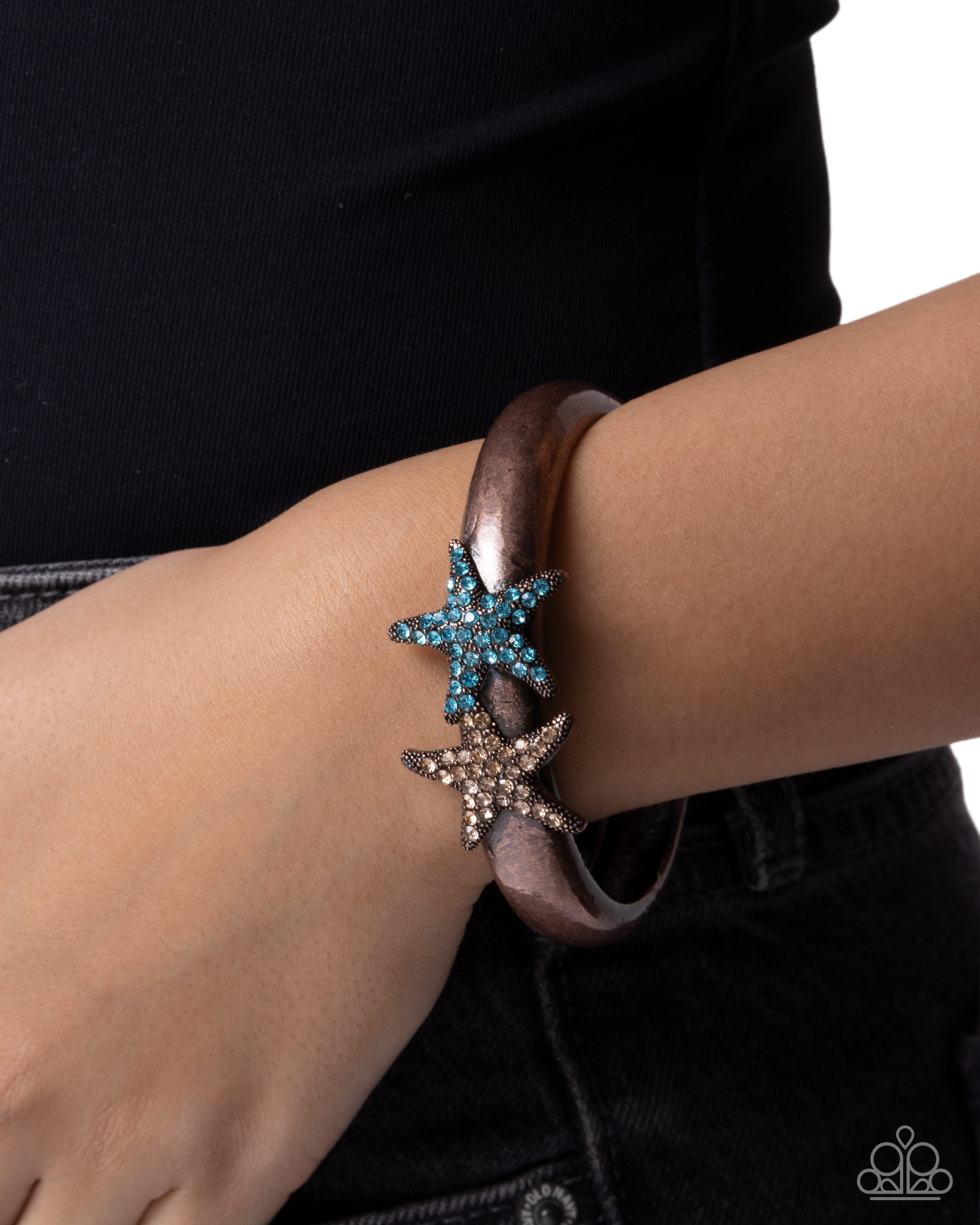 Bracelet with starfish charms on a wrist against a black background