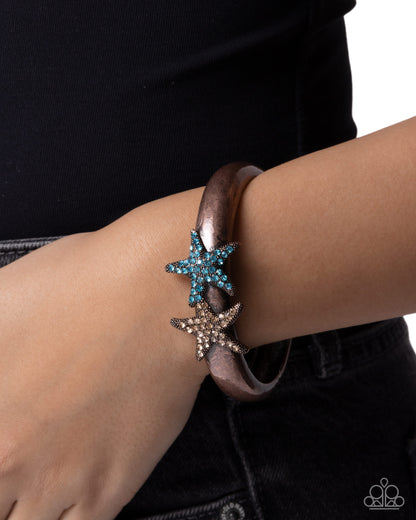 Bracelet with starfish charms on a wrist against a black background