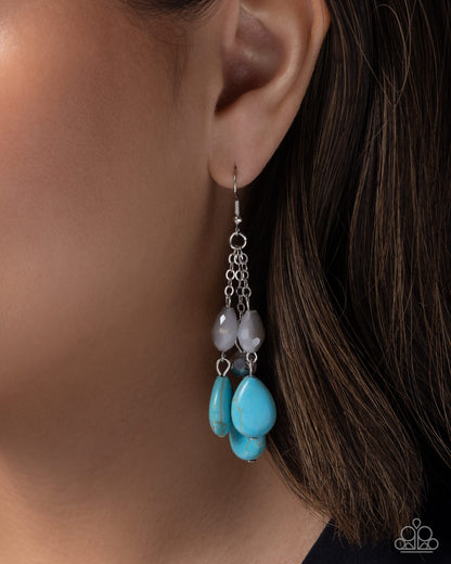 Close-up of an earring with blue teardrop-shaped beads and silver chain on a person's ear.