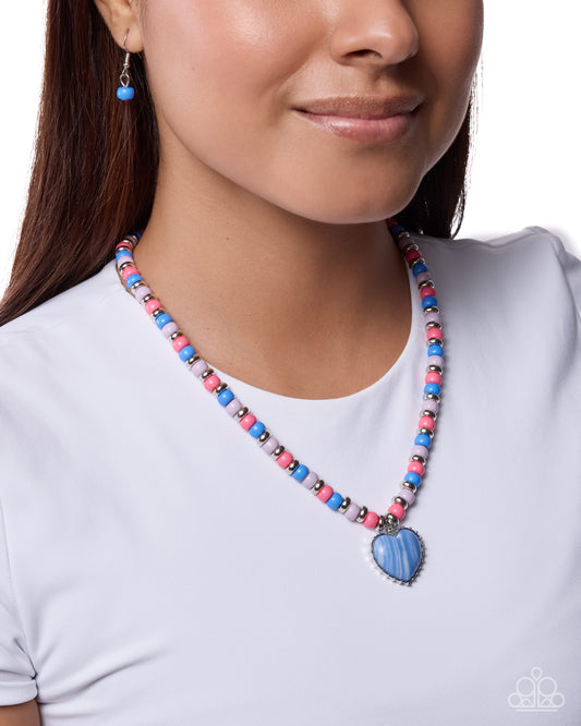 Necklace with a blue heart pendant worn by a person on a white background