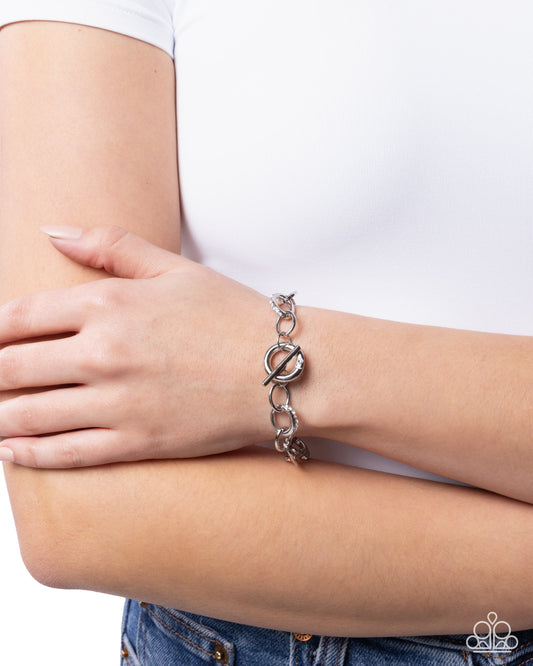 Silver bracelet on a wrist with a plain background