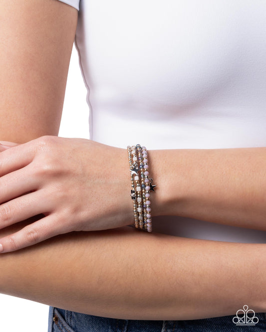 Person wearing a stack of beaded bracelets on a plain background
