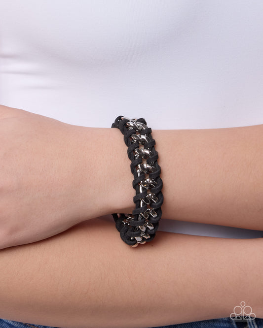 Black braided bracelet with gold accents on a wrist against a white background