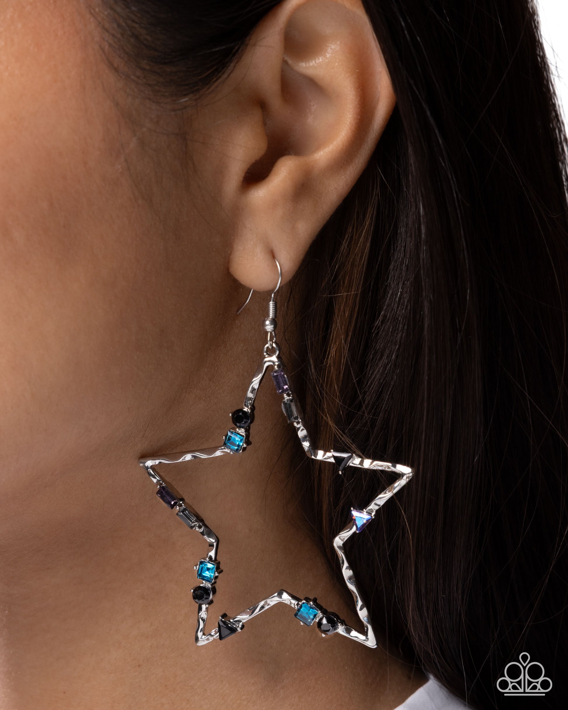 Star-shaped earrings with blue and black gemstones worn by a person.