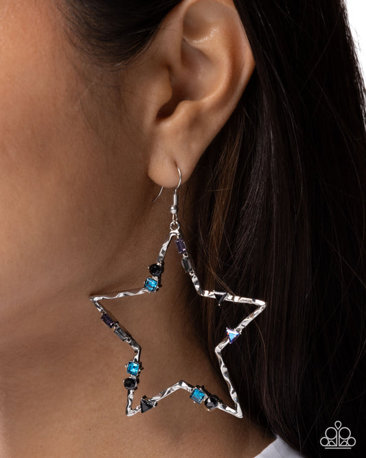 Star-shaped earrings with blue and black gemstones worn by a person.
