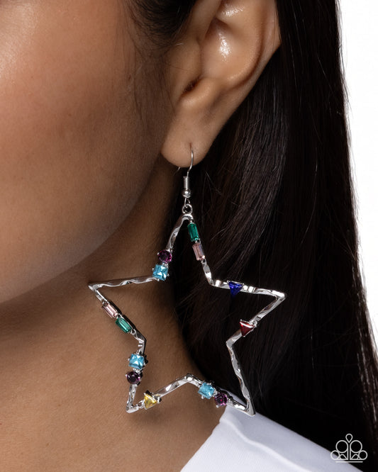 Star-shaped earrings with colorful gemstones worn by a person.
