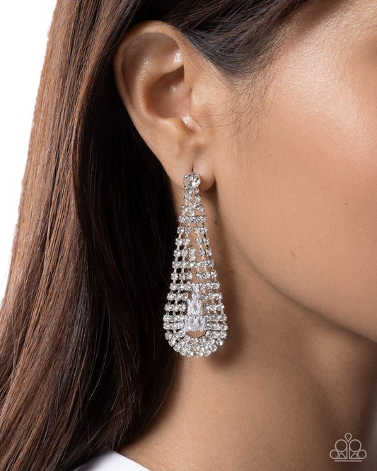 A close-up of a model's ear wearing a teardrop-shaped silver dangle earring adorned with clear rhinestones.