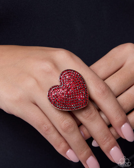 Heart-shaped red gemstone ring on a hand against a black background