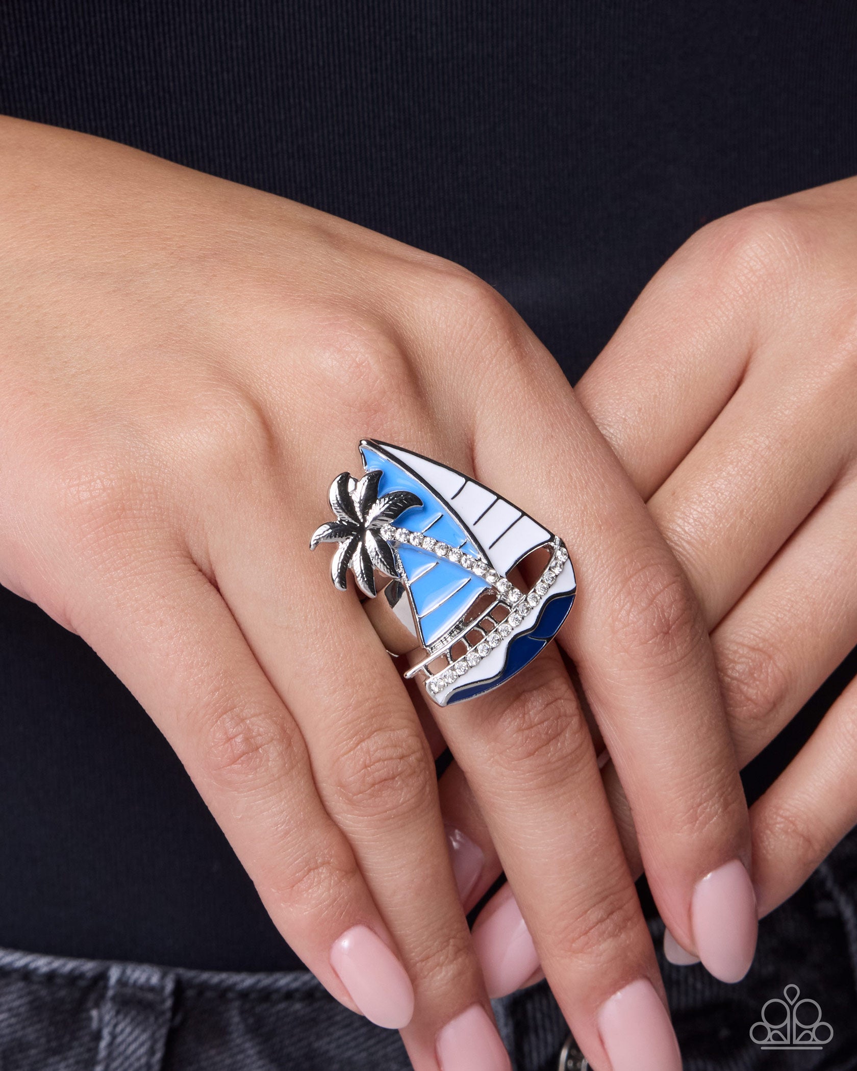 Silver ring with blue and white design on a hand against a black background