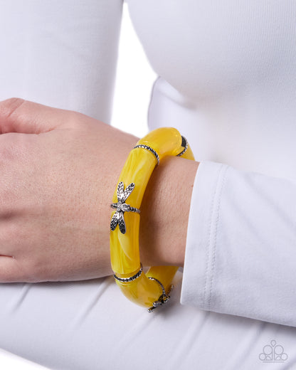 Yellow bracelet with a dragonfly charm on a wrist against a white background