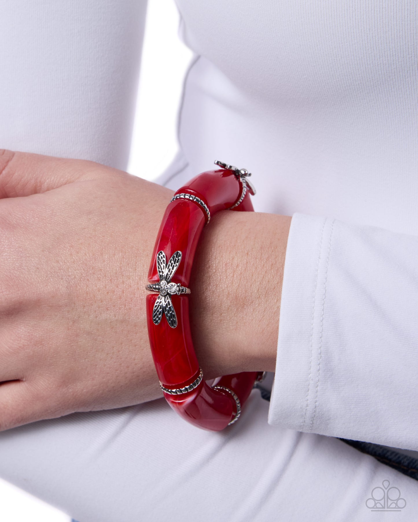 Red bracelet with a silver dragonfly design on a wrist against a white background