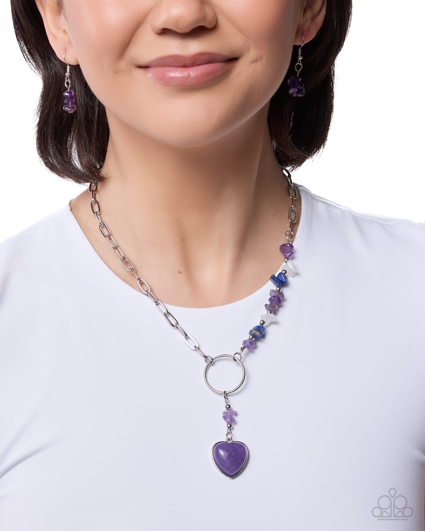 Person wearing a purple heart pendant necklace and matching earrings on a white background