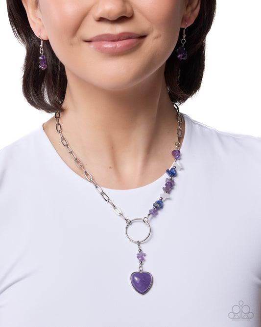 Person wearing a purple heart pendant necklace and matching earrings on a white background