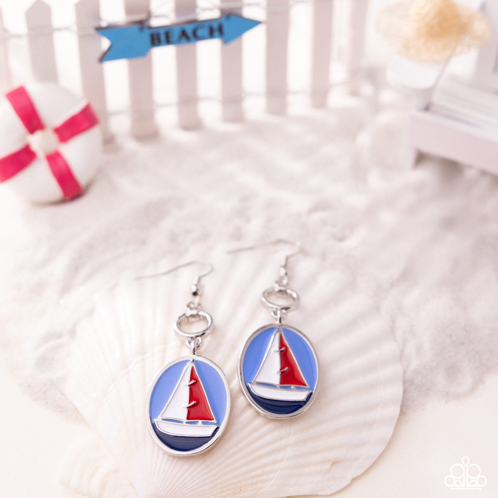 Sailboat earrings on a shell with 'Beach' sign in the background
