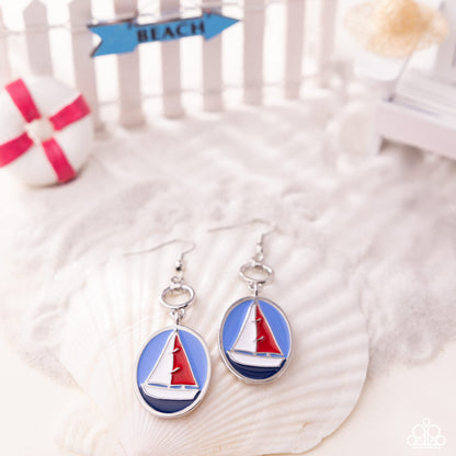 Sailboat earrings on a shell with 'Beach' sign in the background