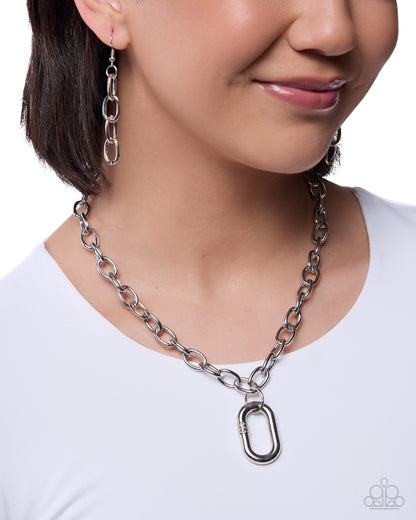 Person wearing a silver chain necklace and earrings on a white background