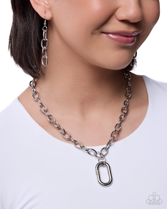 Person wearing a silver chain necklace and earrings on a white background
