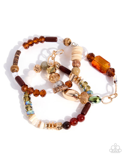 A beaded jewelry set featuring a long beaded necklace and a matching bracelet, crafted with a variety of beads in amber, brown, cream, and gold, accented with a gold clasp and charm, on a white background.