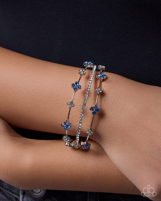 Two silver bracelets with blue stones on a person's wrist against a dark background