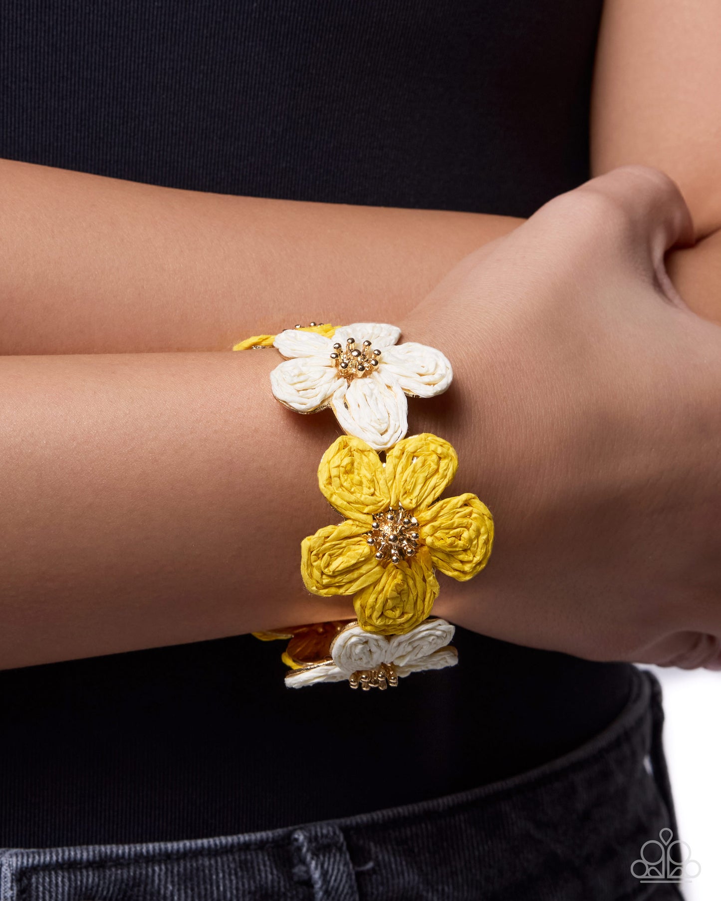 Bracelet with yellow and white floral designs on a wrist against a black background
